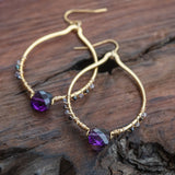 Essence of Enlightenment: Amethyst, Tanzanite, and Rainbow Spinel Earrings in gold and purple, laid beautifully on a table.
