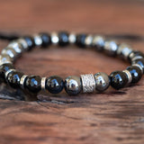 A "Power Protector" bracelet featuring Life Force Hematite and Black Onyx stones with silver accents, laid beautifully on a wooden table.