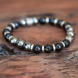 A "Power Protector" bracelet featuring Life Force Hematite and Black Onyx stones with silver accents, laid beautifully on a wooden table.