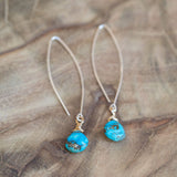 Mixed metal earrings with turquoise stones displayed on a wooden table.
