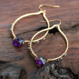 Essence of Enlightenment: Amethyst, Tanzanite, and Rainbow Spinel Earrings in gold and purple, laid beautifully on a table.