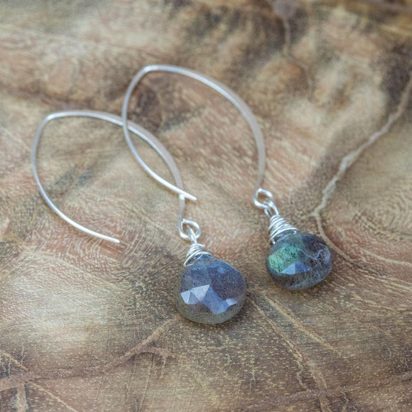 Faceted labradorite silver earrings for personal growth and healing, laid beautifully on a wooden table.