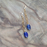 Lapis Lazuli and gold earrings for throat chakra healing, beautifully displayed on a wood table.