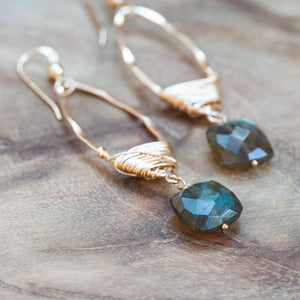 Labradorite long gold wire wrapped earrings elegantly laid on a wooden table, showcasing their shimmer and unique design.