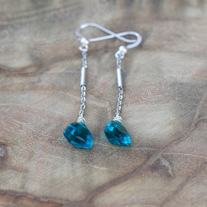 Bright blue crystal earrings on a wooden table, symbolizing peace and tranquility.